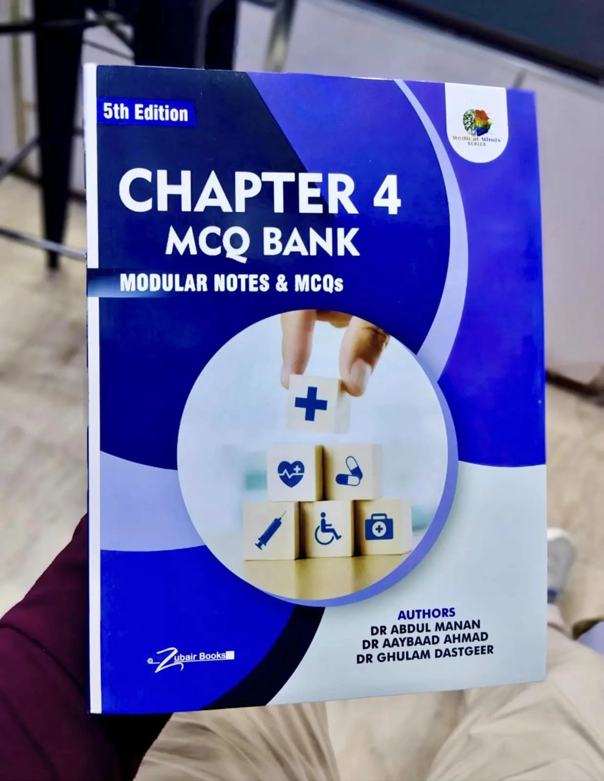 Book titled 'Chapter 4 MCQ Bank' with a blue and white cover held by a person.